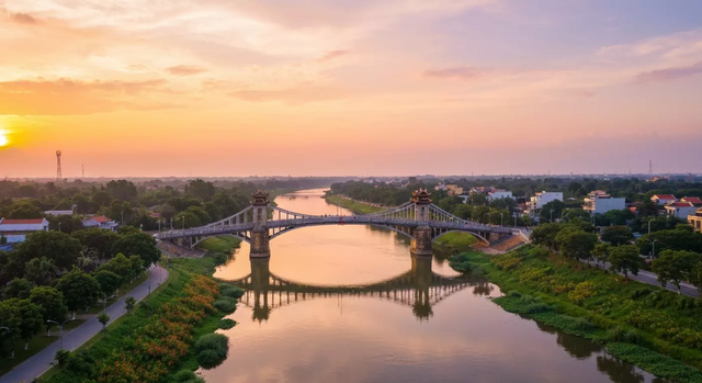 Toàn cảnh Cầu Hiền Lương và Sông Bến Hải từ trên cao lúc hoàng hôn, với ánh sáng vàng rực rỡ, dòng sông êm đềm, bờ cây xanh mướt và cây cầu lịch sử, tạo nên một khung cảnh thanh bình.